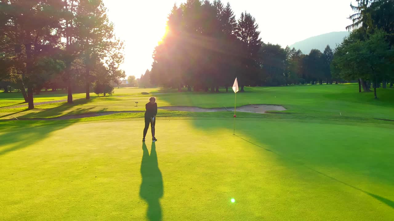 在夕阳下的阴影中，高尔夫球手把高尔夫球放在果岭上视频素材