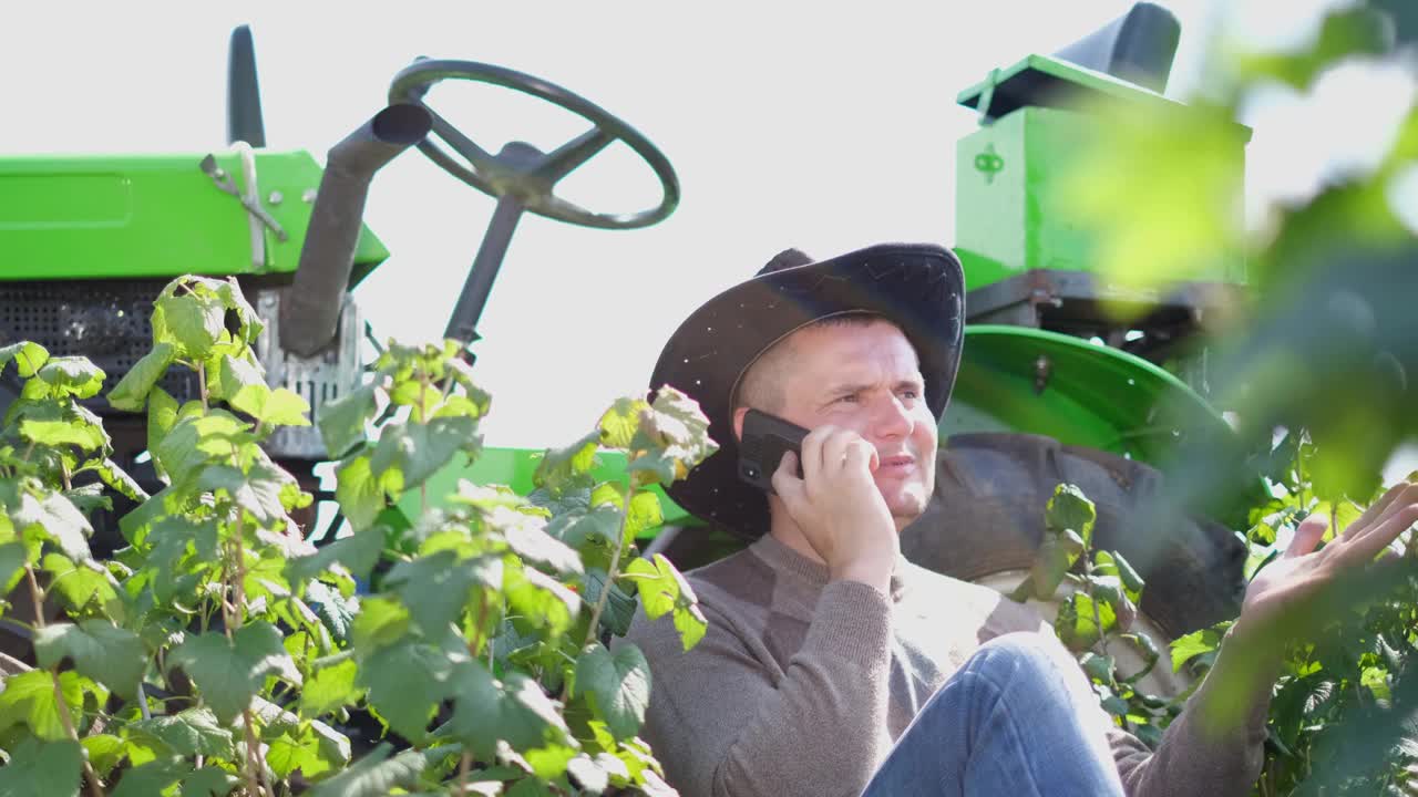 一位年轻的农民正在拖拉机旁休息，他正在使用智能手机。视频下载