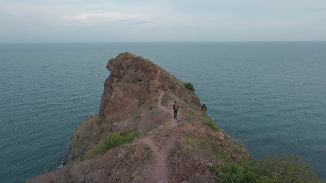 活跃的游客男子背着背包沿着海边的岩石山道行走，从空中拍摄无人机视频下载