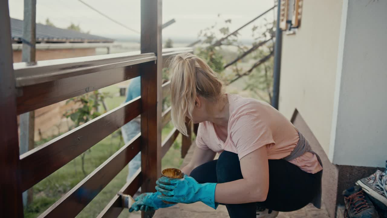 在乡下，一对夫妇正在给他们的房子刷木栅栏视频素材