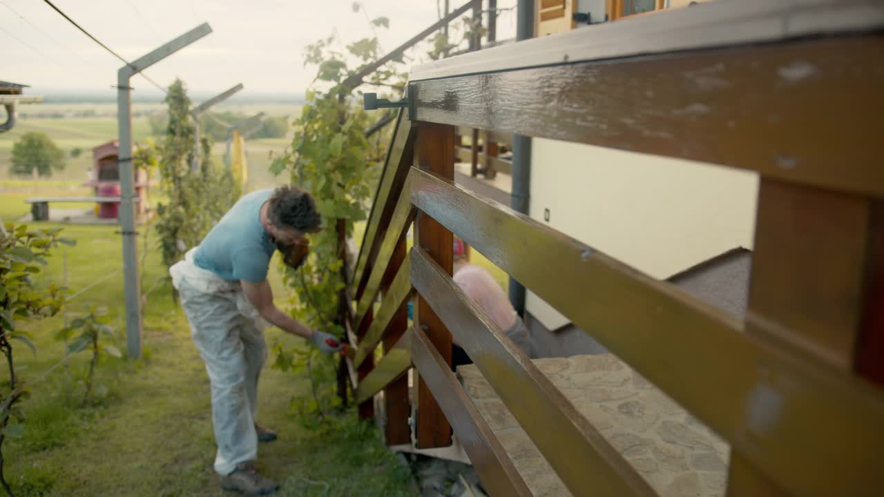 在乡下，一对淘气的夫妇正在给他们的房子刷篱笆视频素材