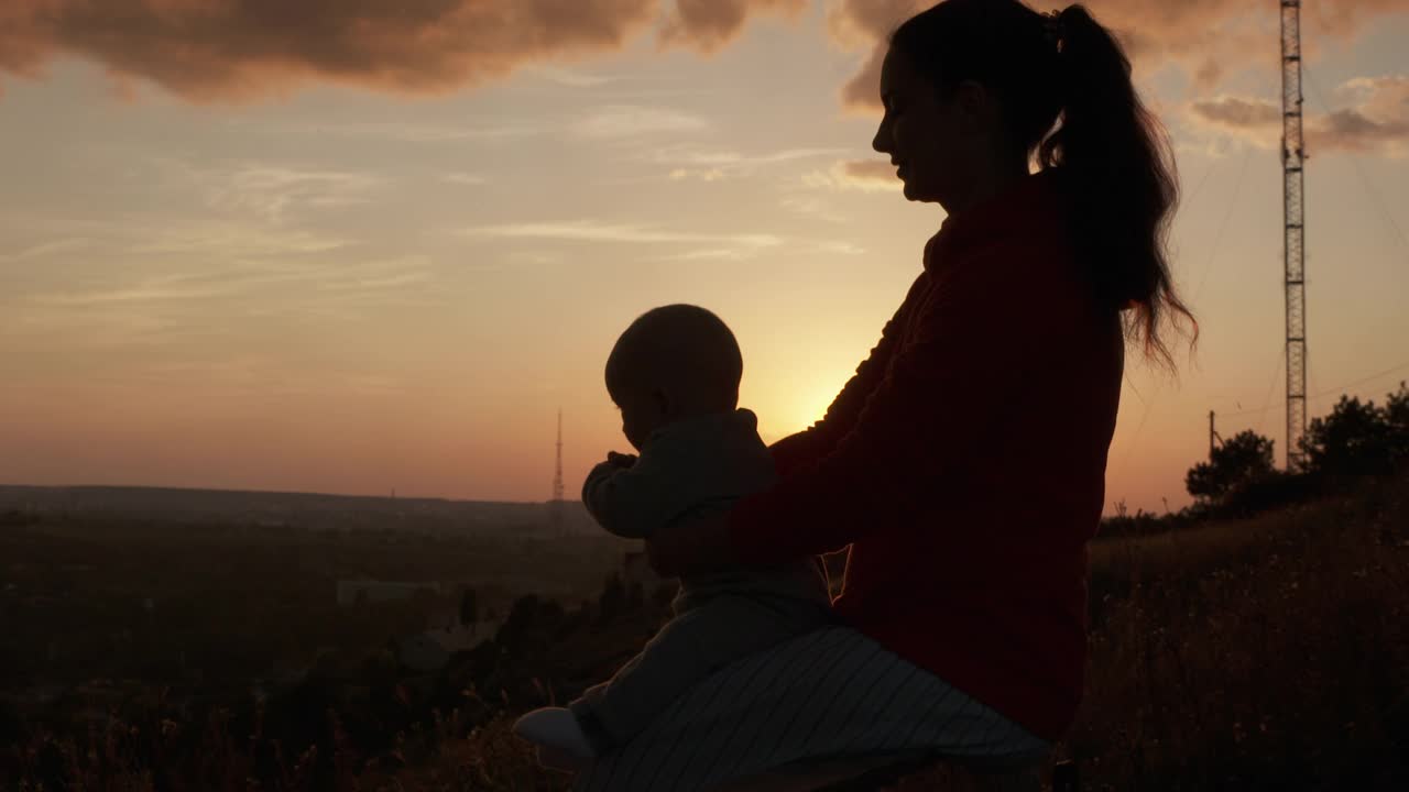 阳光下抱着孩子的女人剪影，快乐的母亲抱着孩子，夕阳背光下抱着孩子的母亲。视频下载