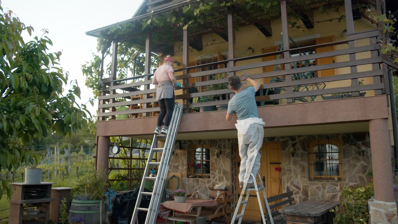 SLO MO夫妇用梯子在房子上漆木栅栏视频素材