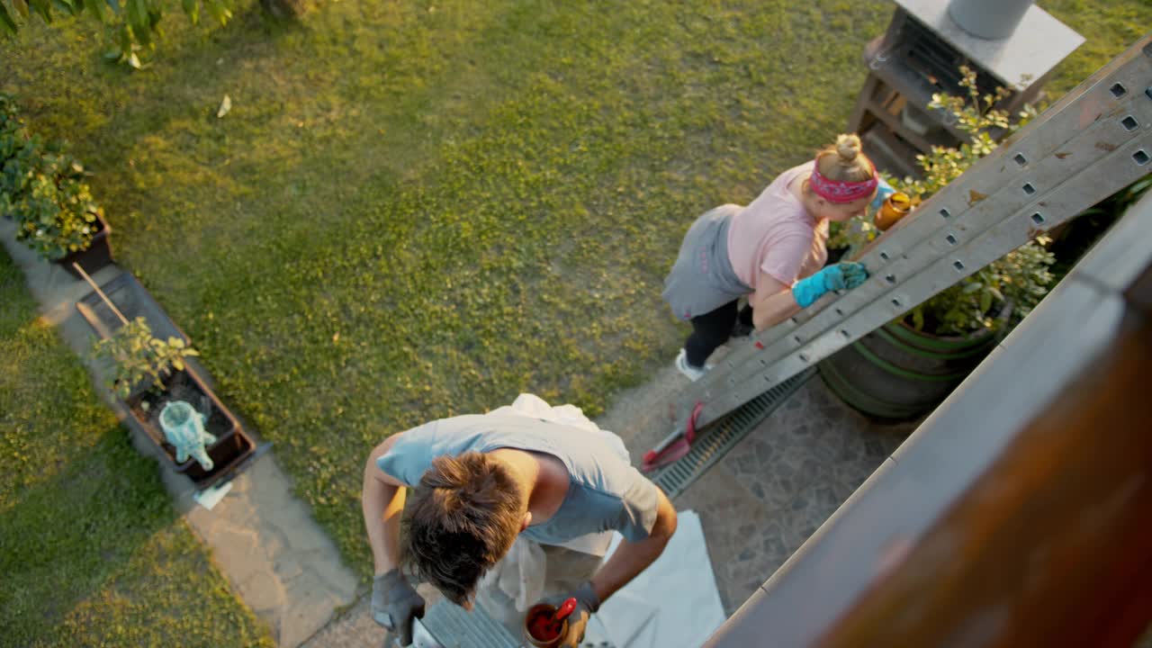SLO MO夫妇用梯子粉刷阳台上的木栅栏视频素材