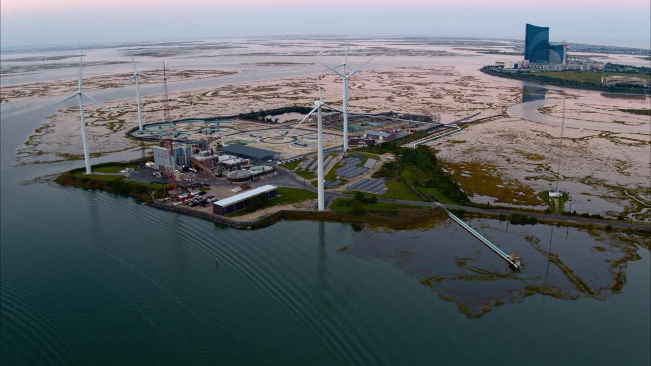 可持续能源用于环境保护。美国新泽西州大西洋城前的一个由风力涡轮机和太阳能板供电的污水处理厂。航拍视频与平移摄像机运动。视频下载