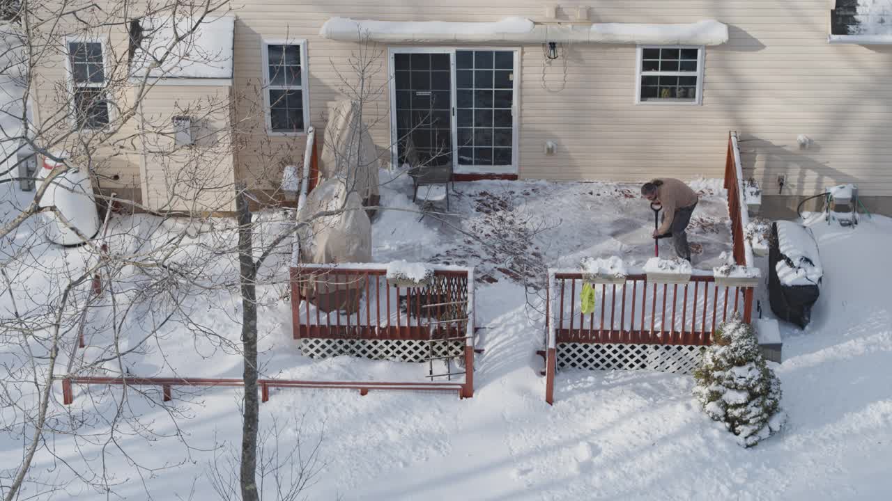 一名成年男子在一场冬季降雪后用铁铲清理门廊上的积雪。鸟瞰无人机视频。视频下载