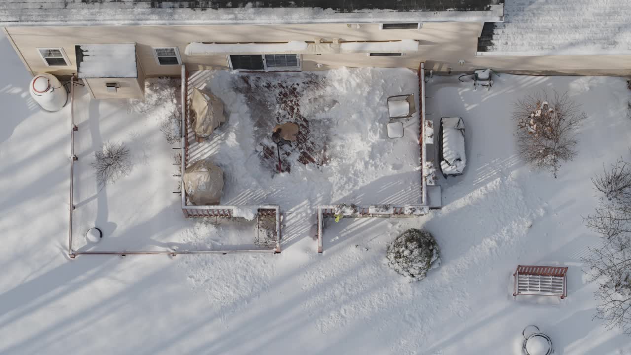 一名成年男子在一场冬季降雪后用铁铲清理门廊上的积雪。鸟瞰直接上方的无人机慢动作视频。视频下载