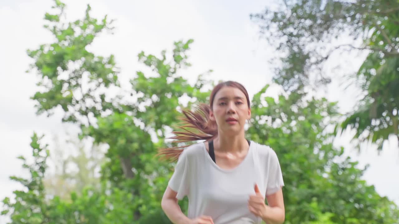 亚洲年轻美丽的运动女子在公园的街道上跑步。美丽的运动员，健美的女孩穿着运动服，在傍晚日落的花园中进行户外慢跑健身保健。视频素材