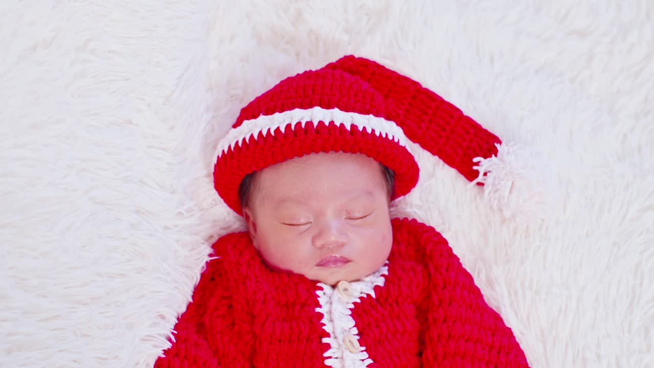 可爱的新生儿穿着圣诞老人的服装躺着睡觉，等待着庆祝圣诞和新年快乐。平静的婴儿婴儿睡在红色的圣诞老人布视频下载