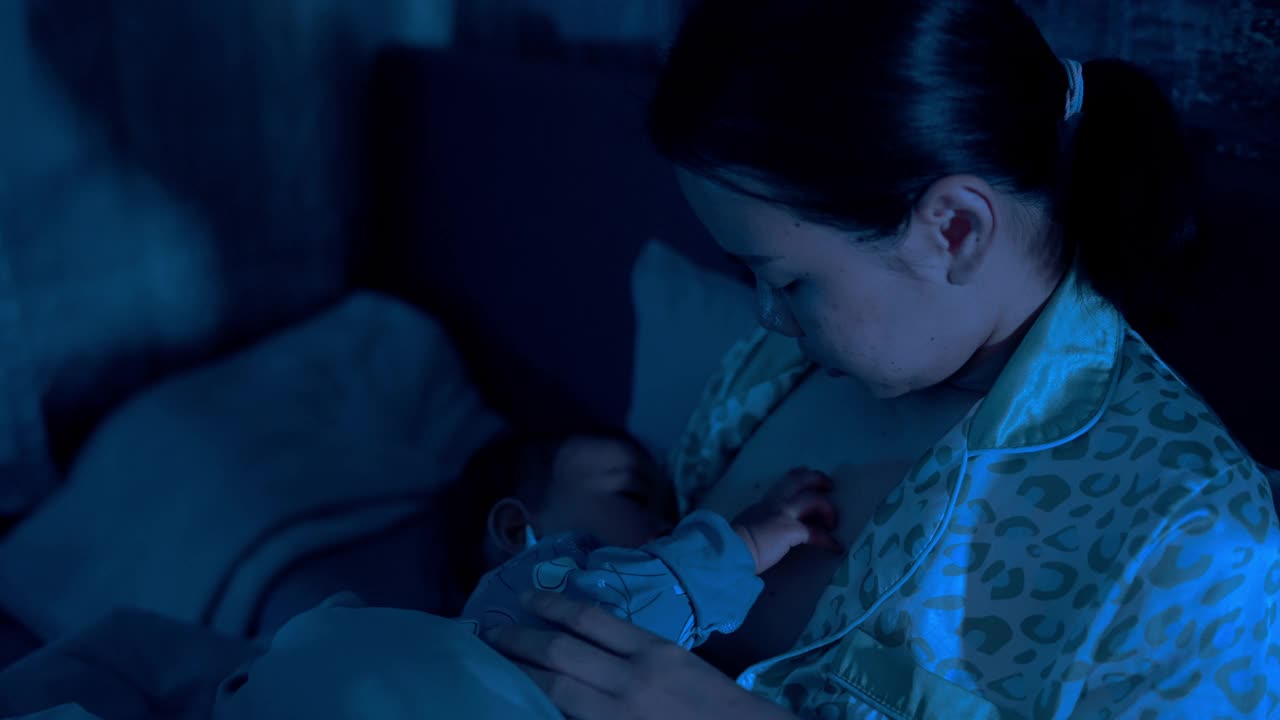 亚洲母亲正面情绪哺乳女儿和使用电话与产后深夜在床上的概念视频下载