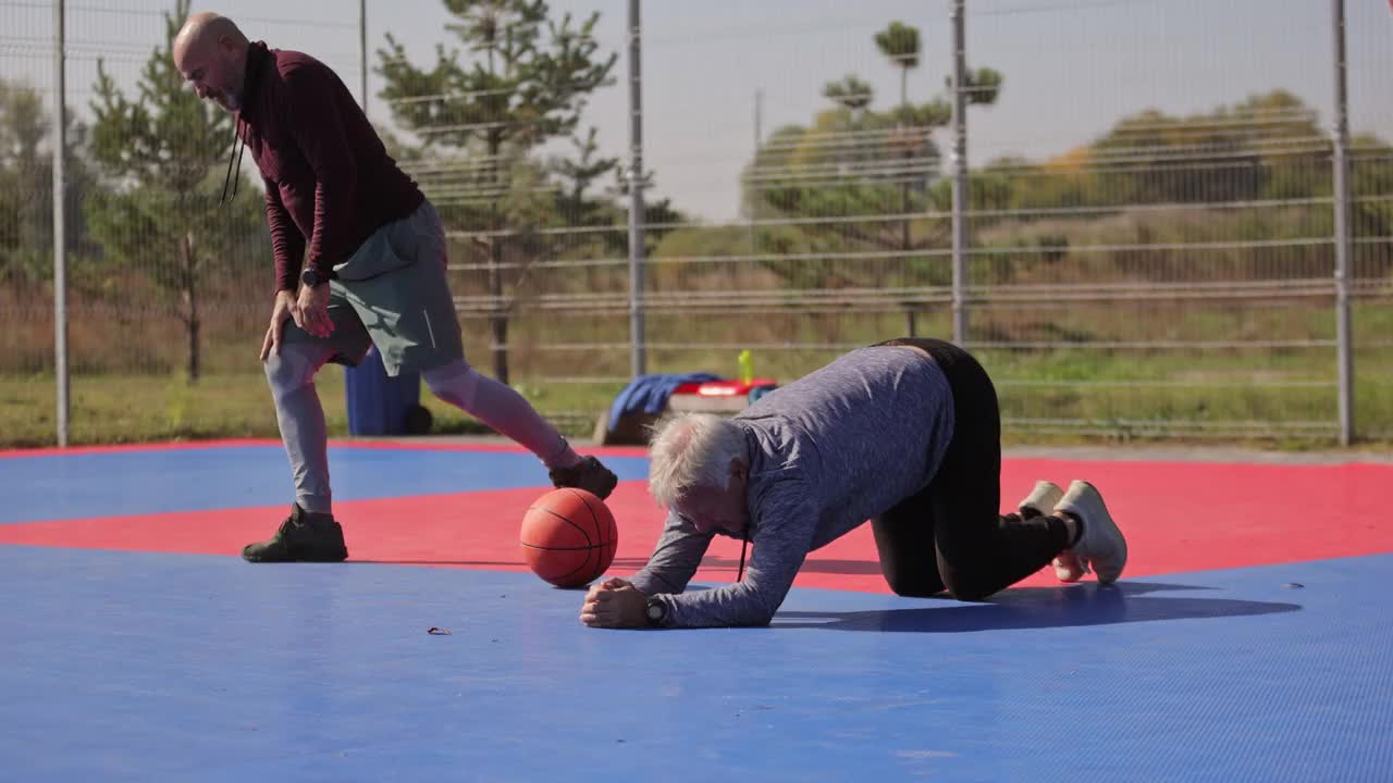 两个年长的朋友在室外篮球场打篮球前伸展身体视频素材
