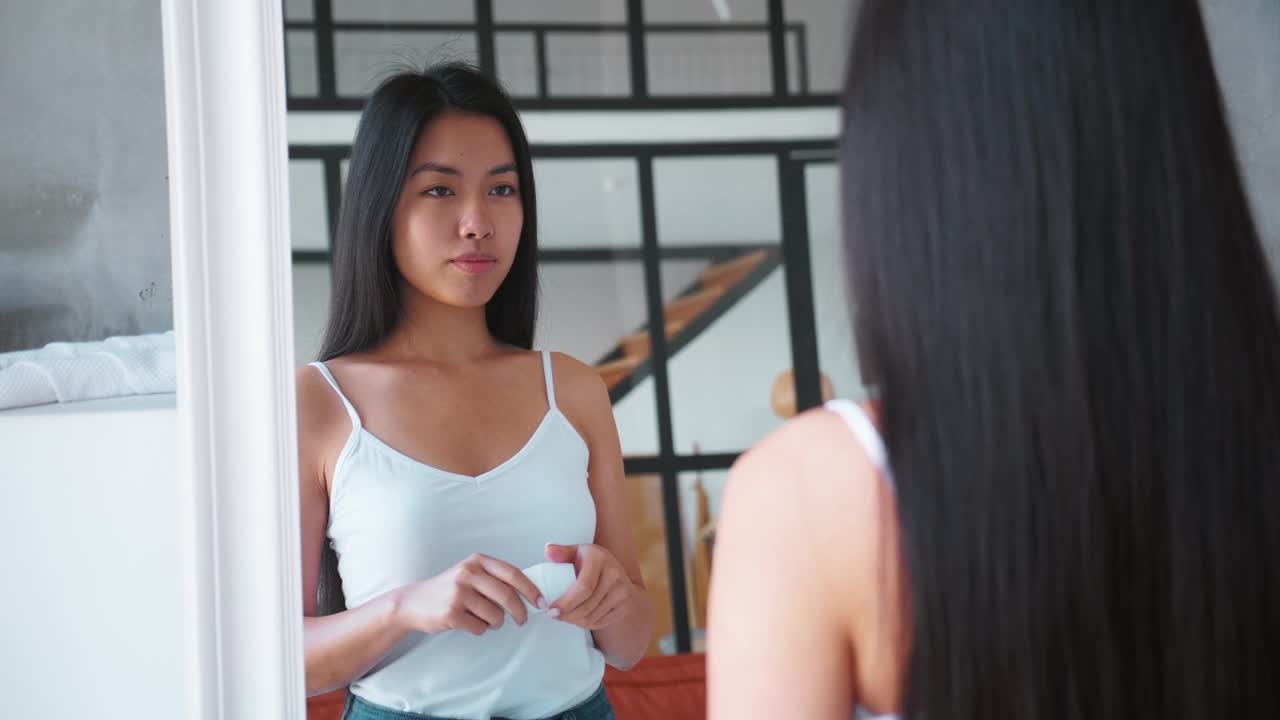 美丽的亚洲女人感到享受和幸福，微笑着在家里看着她的镜子，在腋窝上使用止汗除臭剂。日常卫生习惯。身体护理的概念视频下载