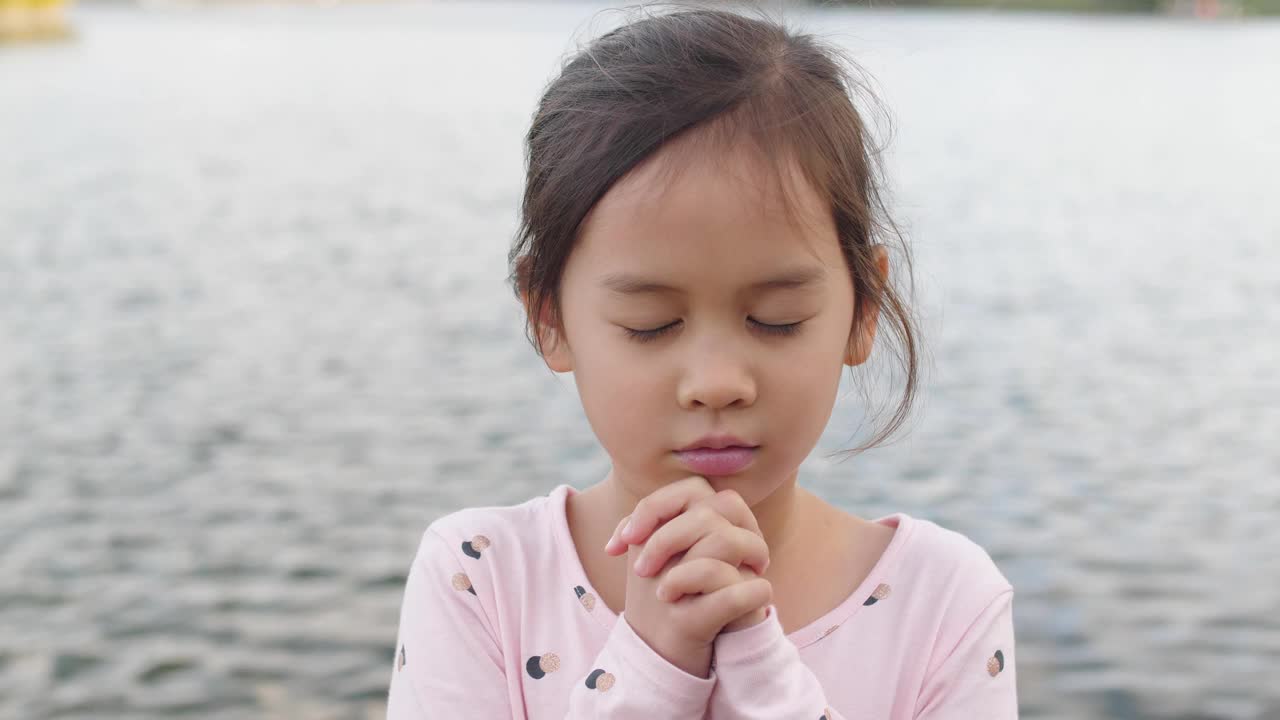 4K慢镜头的年轻混血亚洲女孩在户外湖祈祷，儿童闭着眼睛祈祷，在线家庭教堂视频下载
