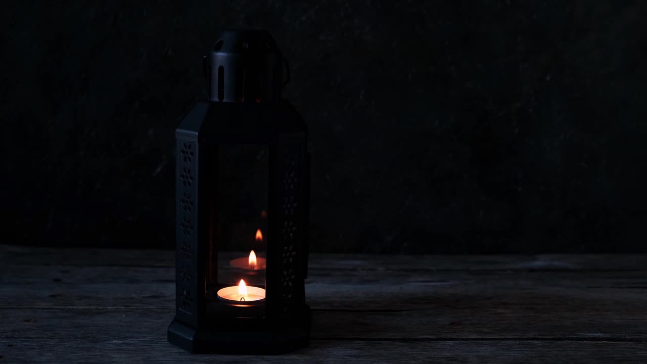 在黑暗的房间里，木桌上放着一盏点着蜡烛的复古灯。视频素材