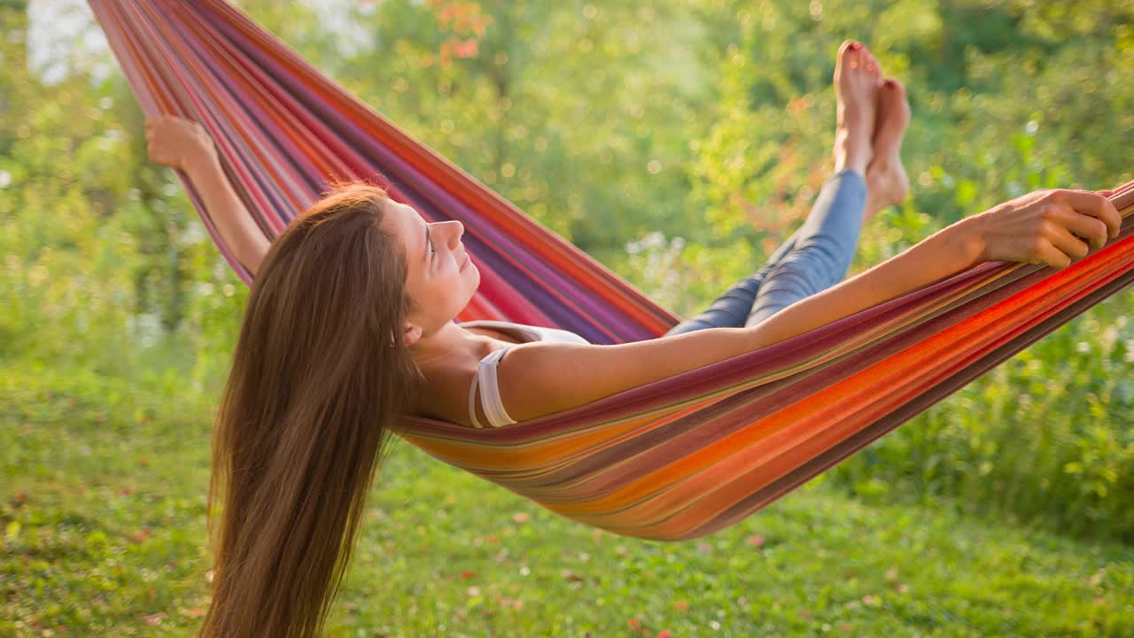 快乐的年轻女子在后院树下的吊床上荡秋千，对着镜头笑着玩视频下载