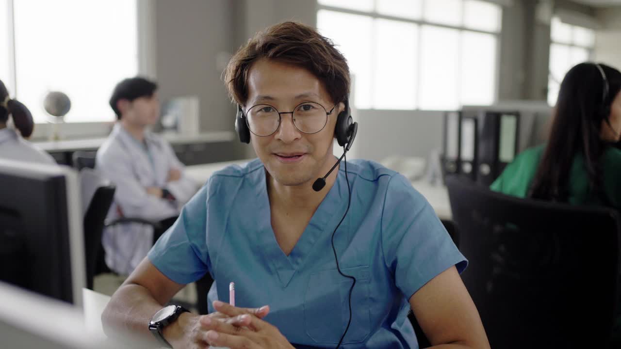 在呼叫中心办公室里，一位亚洲医生看着摄像机和视频通话中药物和补充剂的使用情况。视频下载