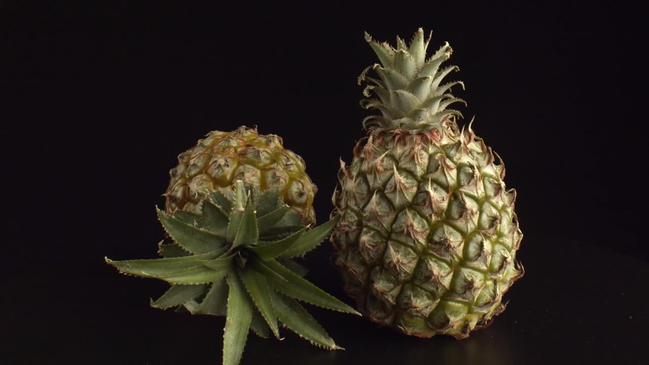 两个美丽的菠萝在黑色背景下。大的果实类似于针叶球果。菠萝水果富含维生素。健康食品的概念。视频素材