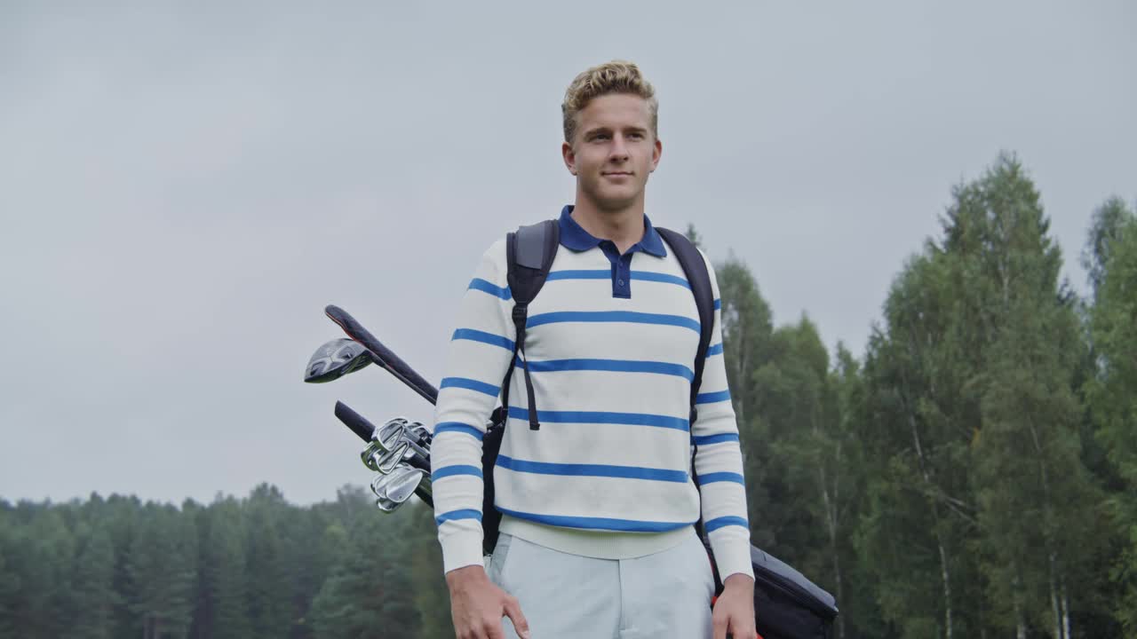 一个年轻人穿着运动服，背后背着高尔夫器材，看着摄像机视频下载