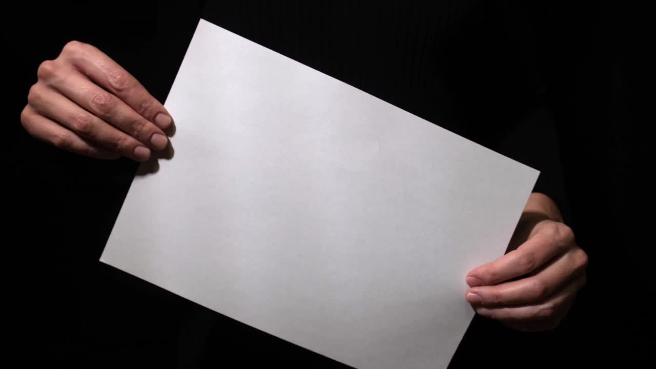手拿空白的白纸在黑色的背景上，旋转它和静止，适合文本，广告和介绍视频素材