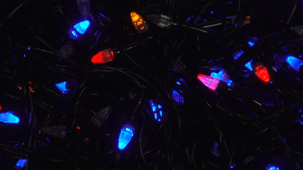 五颜六色的圣诞灯泡花环在黑暗中闪烁。视频下载