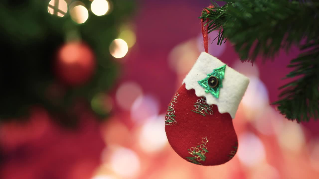 红色装饰装饰袜子挂在圣诞树的树枝上，壁炉的火焰在背景中模糊，五颜六色的灯光散景。圣诞节装饰的想法和快乐的节日结束的一年。视频素材