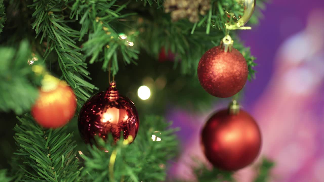 红色装饰球挂在圣诞树的树枝上，壁炉的火焰在背景中模糊，彩灯散景。圣诞节装饰的想法和快乐的节日结束的一年。视频素材