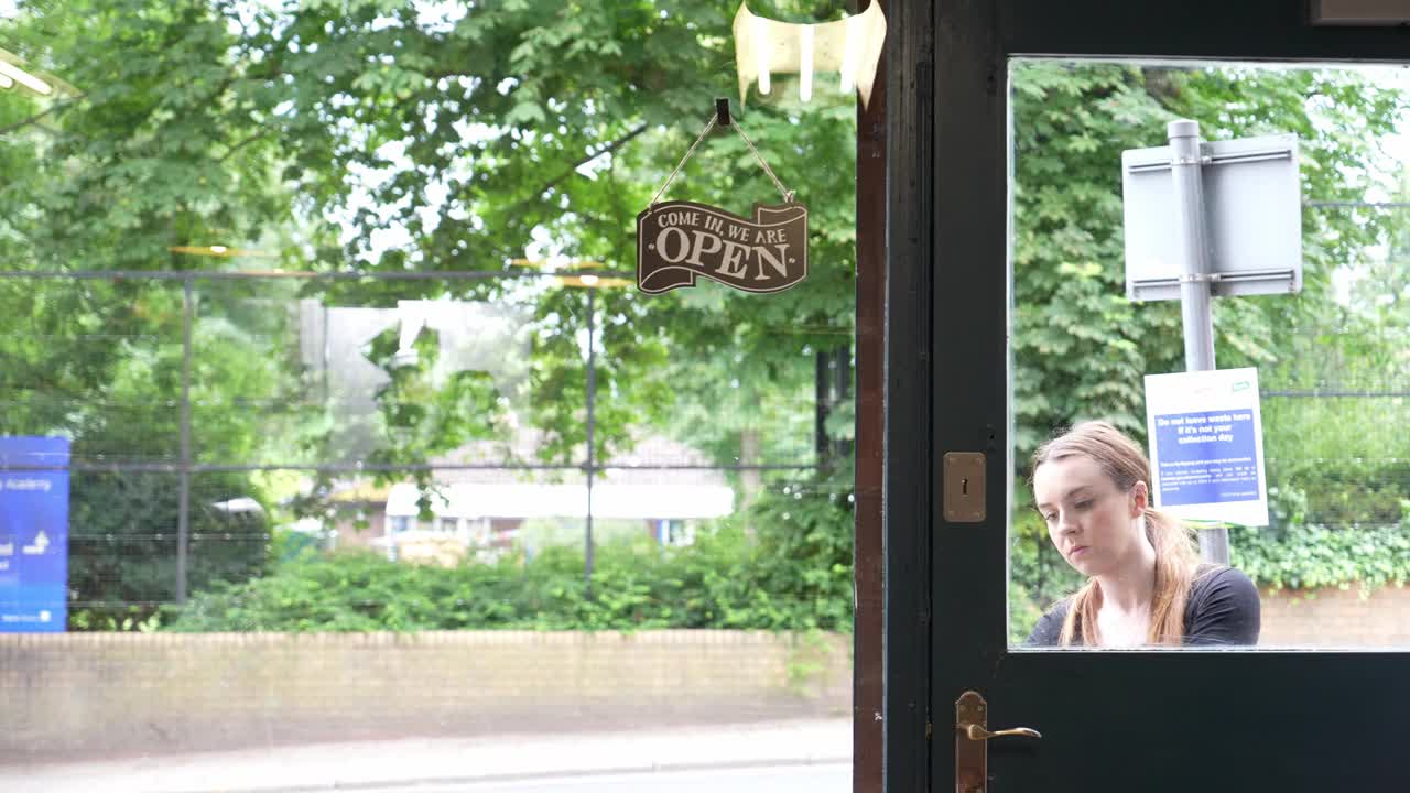 一个女人戴上围裙，打着营业牌开门视频下载