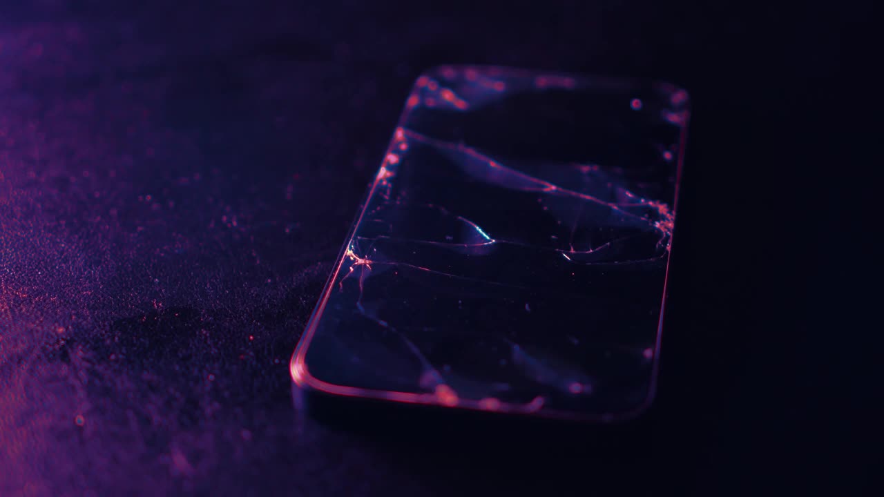 黑色纹理背景下的碎玻璃智能手机屏幕。闪烁着彩虹般的光芒。屏幕上有裂纹的玻璃。修复,遗憾的概念。选择性聚焦，近距离，4K视频素材