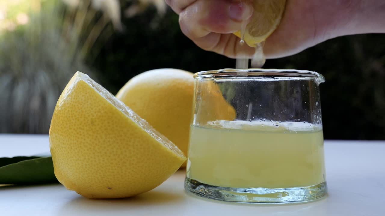 柠檬被挤进一个玻璃瓶，制成纯柠檬汁。背景镜头健康的生活方式视频下载