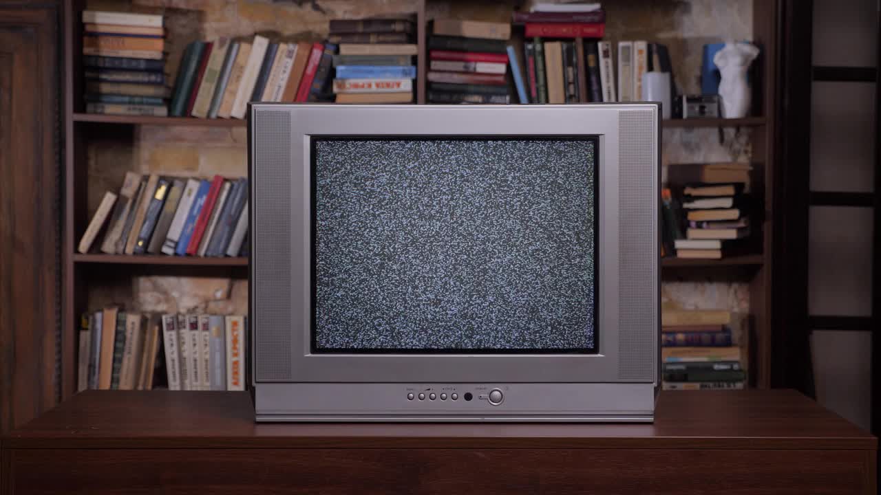 以旧书为背景的复古电视机。电视信号噪声差。房间里有一台旧电视机。90年代复古电视屏幕静电噪音。模拟静态效果复古电视室内家庭图书馆书架背景视频下载