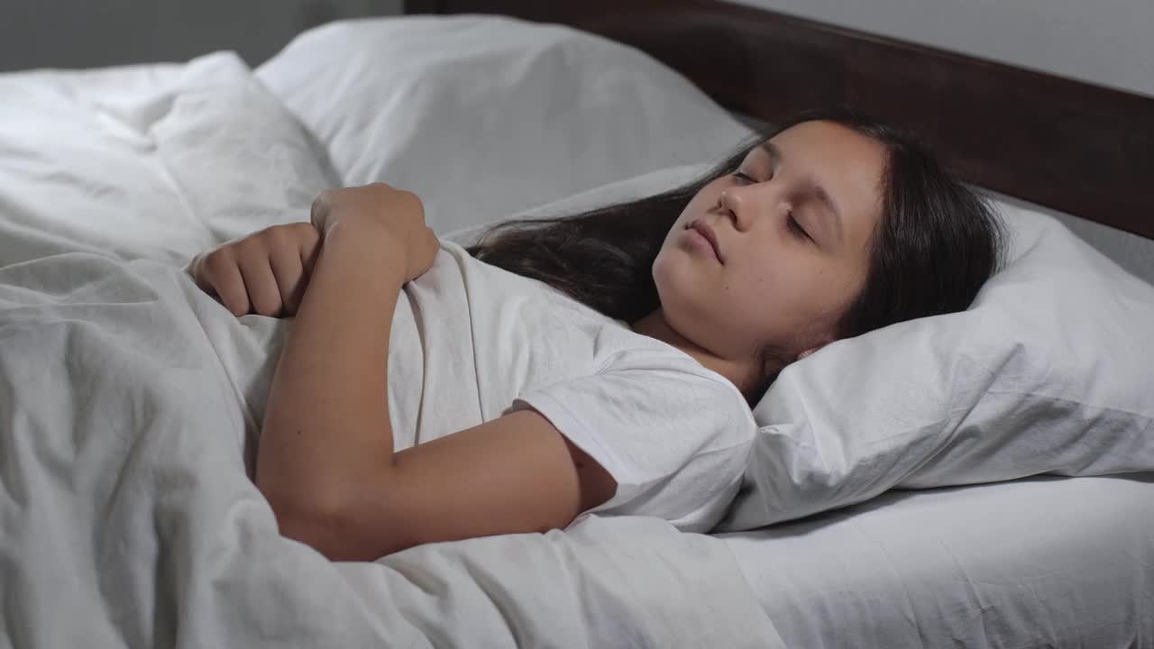 特写的女孩9岁长棕色头发睡在床上与白色亚麻在明亮的房间。失眠概念4 k。睡眠不宁的青少年视频下载
