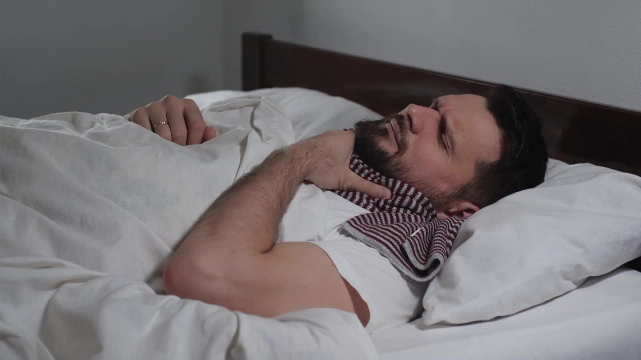 特写的白人大胡子男子感冒了，躺在浅色房间的床上，穿着白色的亚麻布，患流感。有魅力的家伙咳嗽打喷嚏4K视频下载