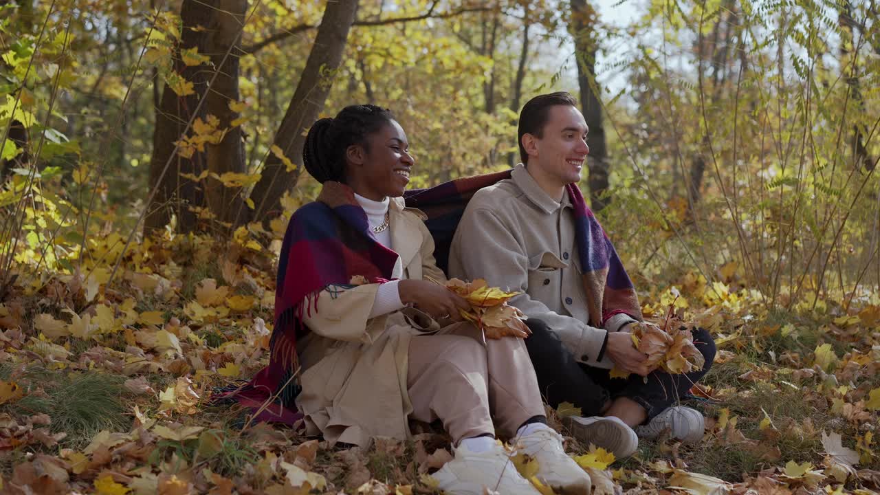 秋天，在公园里，一对赛车夫妇坐在毯子上，把树叶抛向空中视频素材