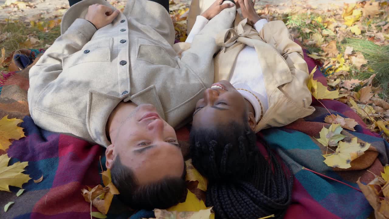秋天，在公园里，一对混合赛跑的夫妇躺在毯子上视频素材