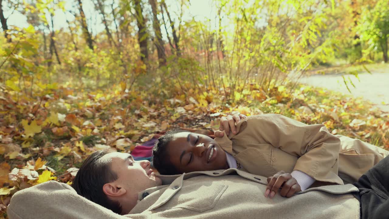 秋天，在公园里，一对混合赛跑的夫妇躺在毯子上视频下载