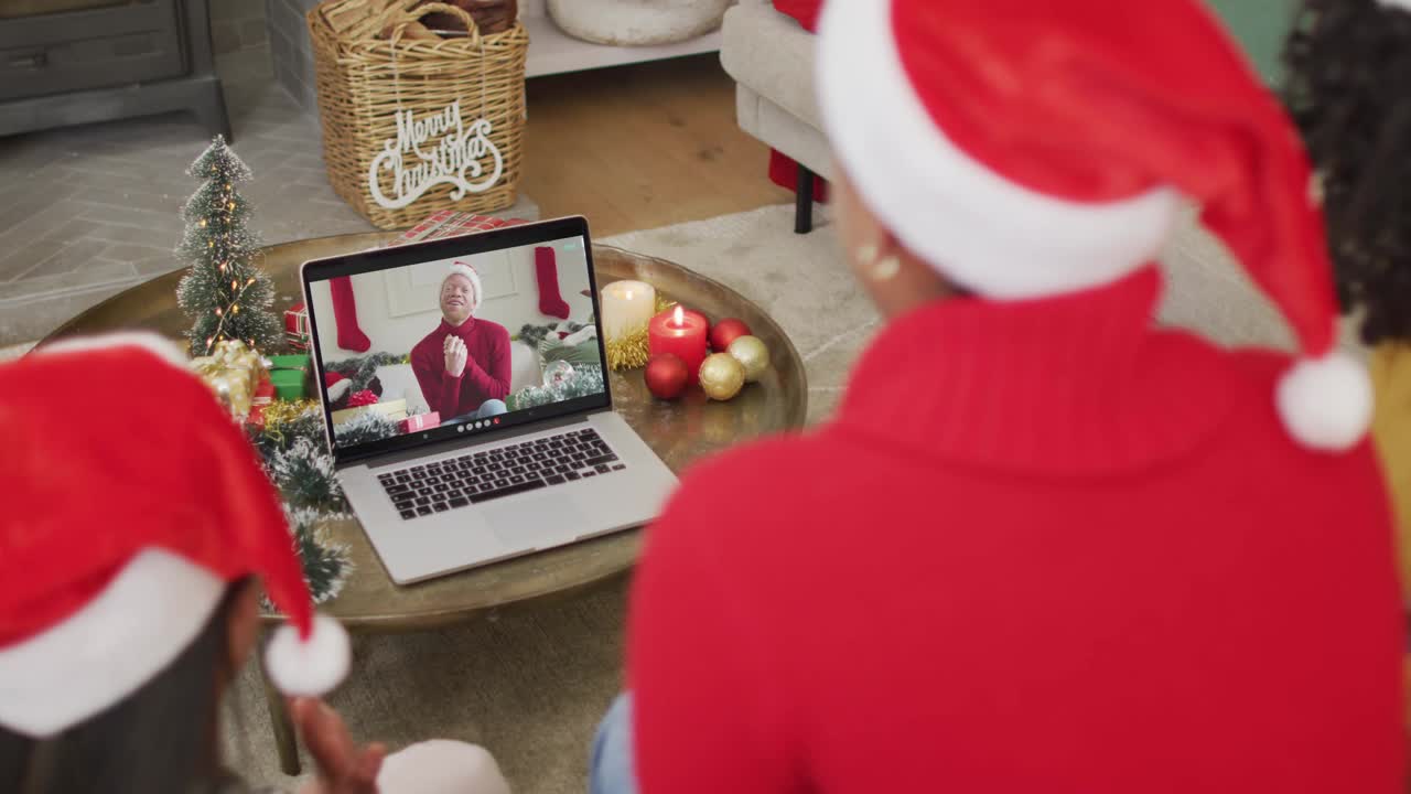戴着圣诞帽的非洲裔美国家庭使用笔记本电脑与屏幕上的男人进行圣诞视频通话视频下载