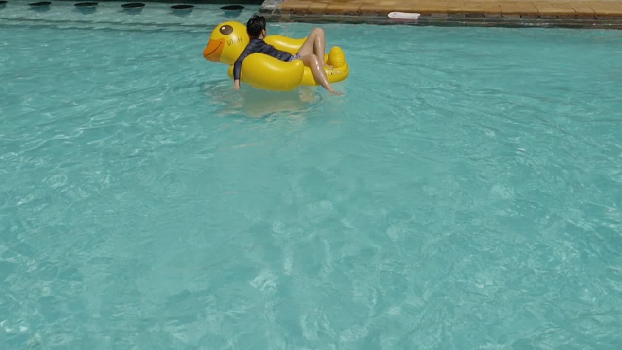 快乐的亚洲男孩和女孩一起在游泳池的黄鸭子橡皮筏上放松，与家人一起度假，生活理念。视频素材
