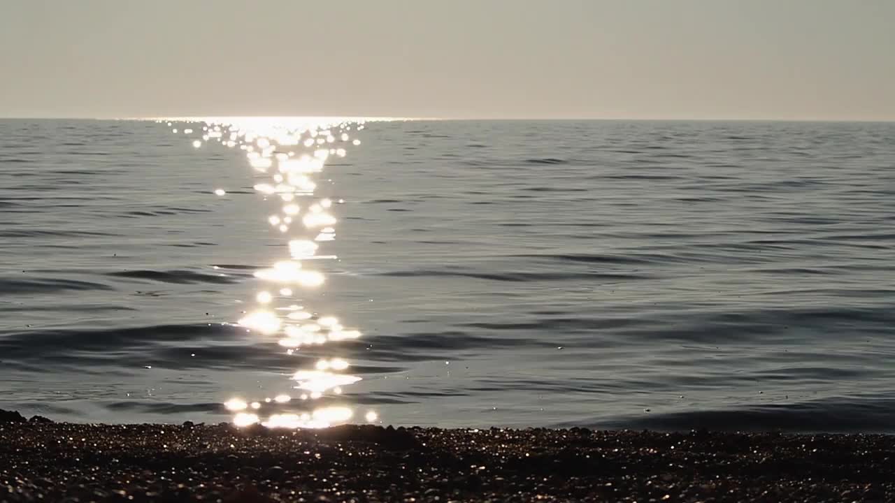 阳光照射在海水上，伴随着海浪的小波纹和轻柔的海浪声。海景。美丽的水面与岸边的边缘。海洋背景视频素材