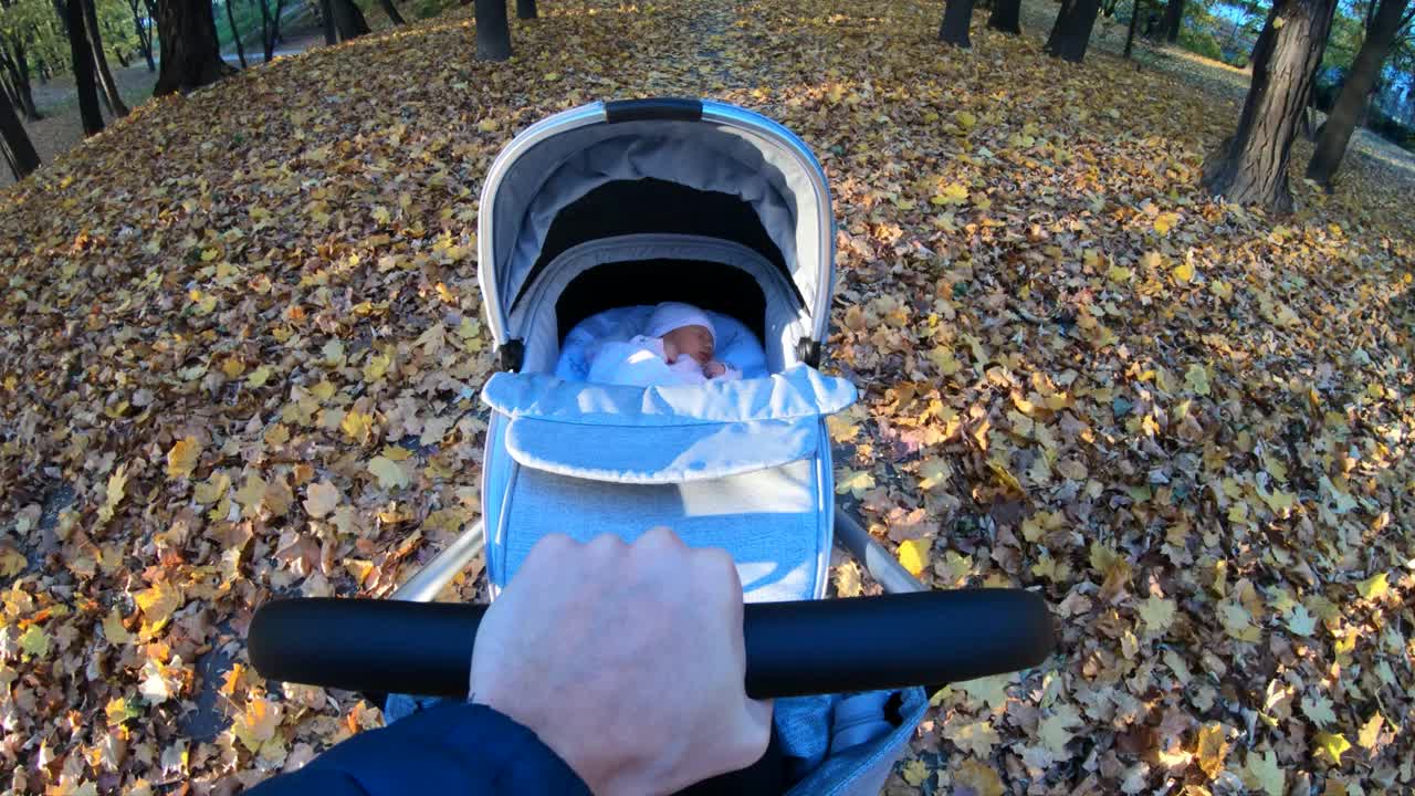 一名男子在公园里推着一辆婴儿车，照片拍摄于秋天视频下载
