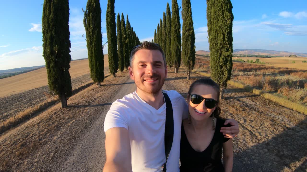 意大利托斯卡纳，一对幸福的夫妇沿着柏树成行的道路散步视频下载