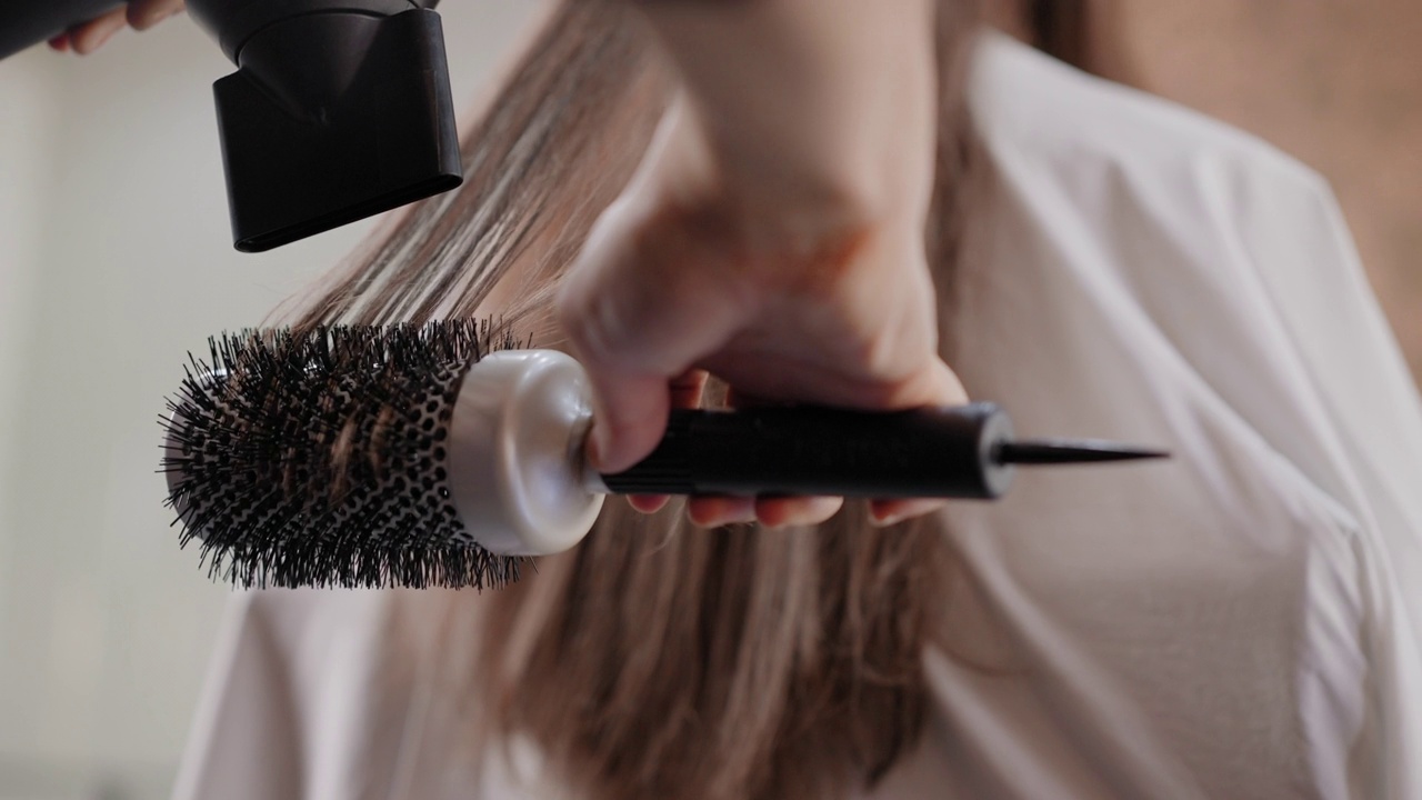 近距离的发型师的手使用吹风机使客户的头发拉直和干燥在发廊后，高光和剪新发型。视频素材