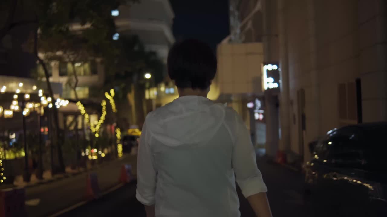 后视图亚洲华人中年妇女戴着防护口罩在夜晚的城市中行走视频素材