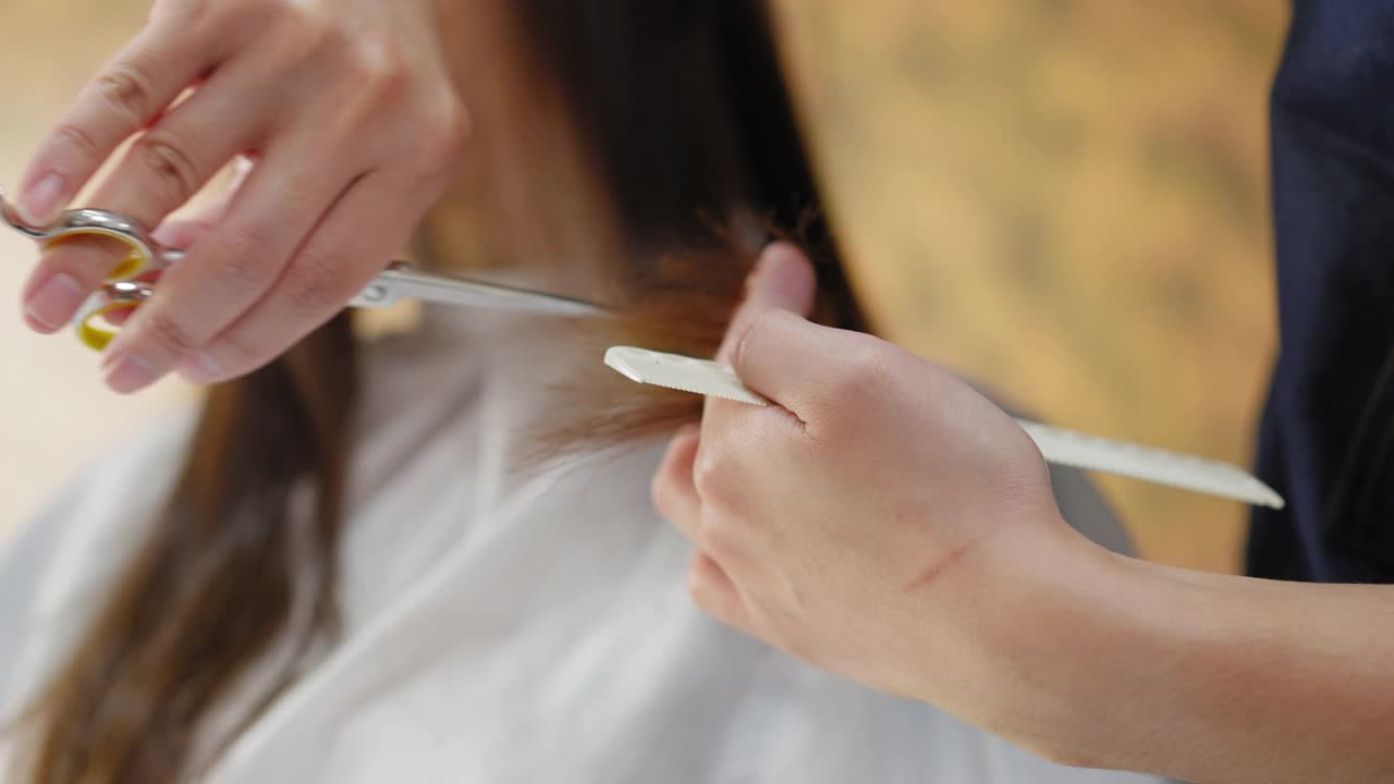 近距离的专业造型师的手修剪分叉末端在女性的头发在沙龙。美发师在美容院为客户剪发。去除分叉。视频素材