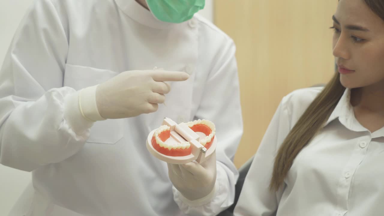 一名白人牙医在医院诊所向亚洲病人示范如何使用牙线。清洗。医生。牙科，医疗和健康。视频下载