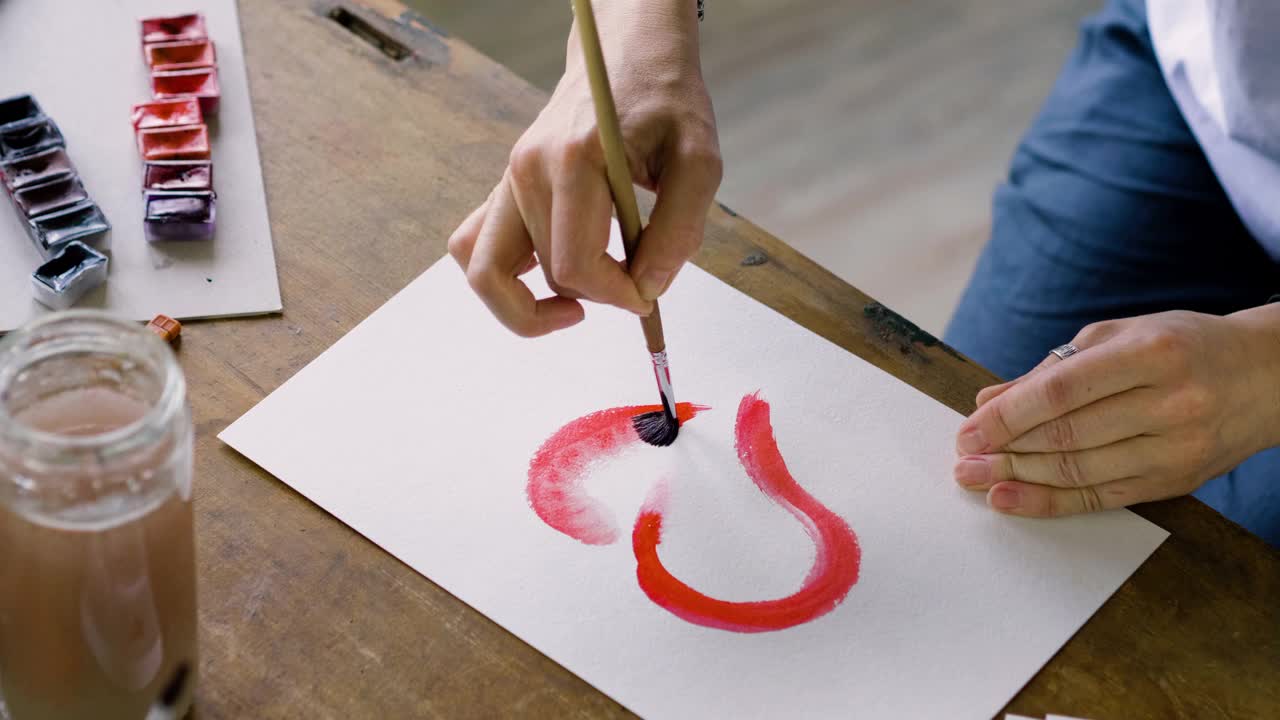 女艺术家的手在水彩中画一颗红心的特写镜头。4 k视频下载