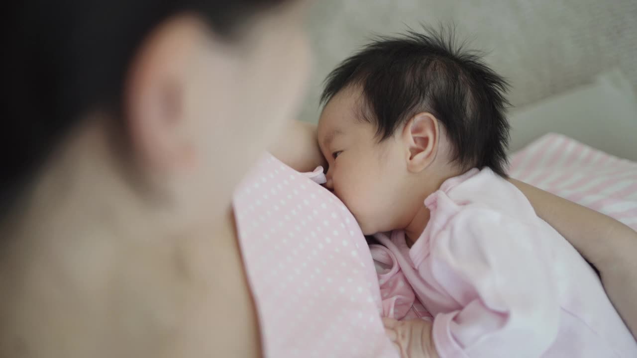 年轻的亚洲母亲正在哺乳她的孩子。视频下载