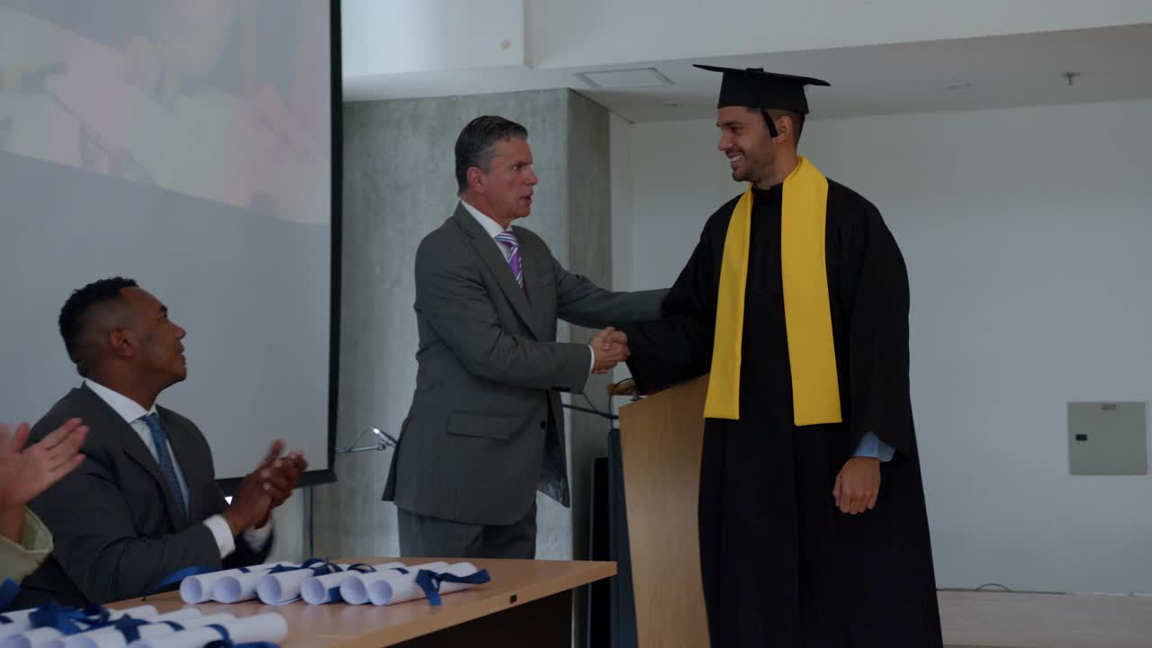 在毕业典礼上，一名骄傲的男学生接受了他的毕业证书，他与所有的老师握手，然后看着他的同学举起了手视频下载