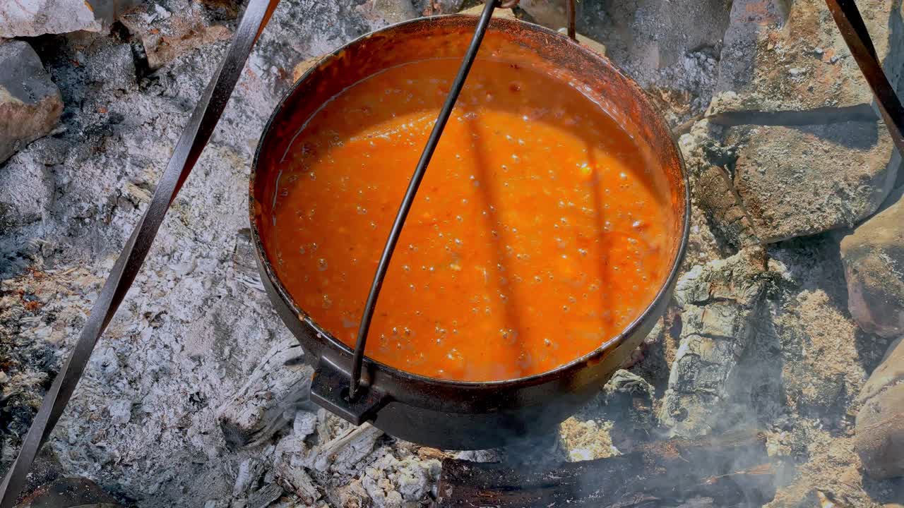 POV人在篝火上搅拌着铸铁锅里冒着泡泡的炖肉视频下载