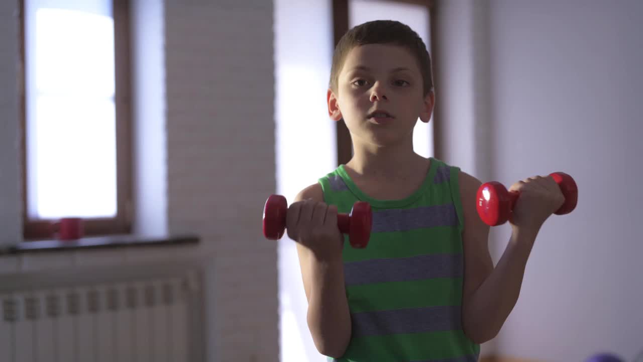 健康活跃的高加索小强壮的男孩在条纹背心举重哑铃在室内家庭运动肌肉训练娱乐健身锻炼休闲视频素材