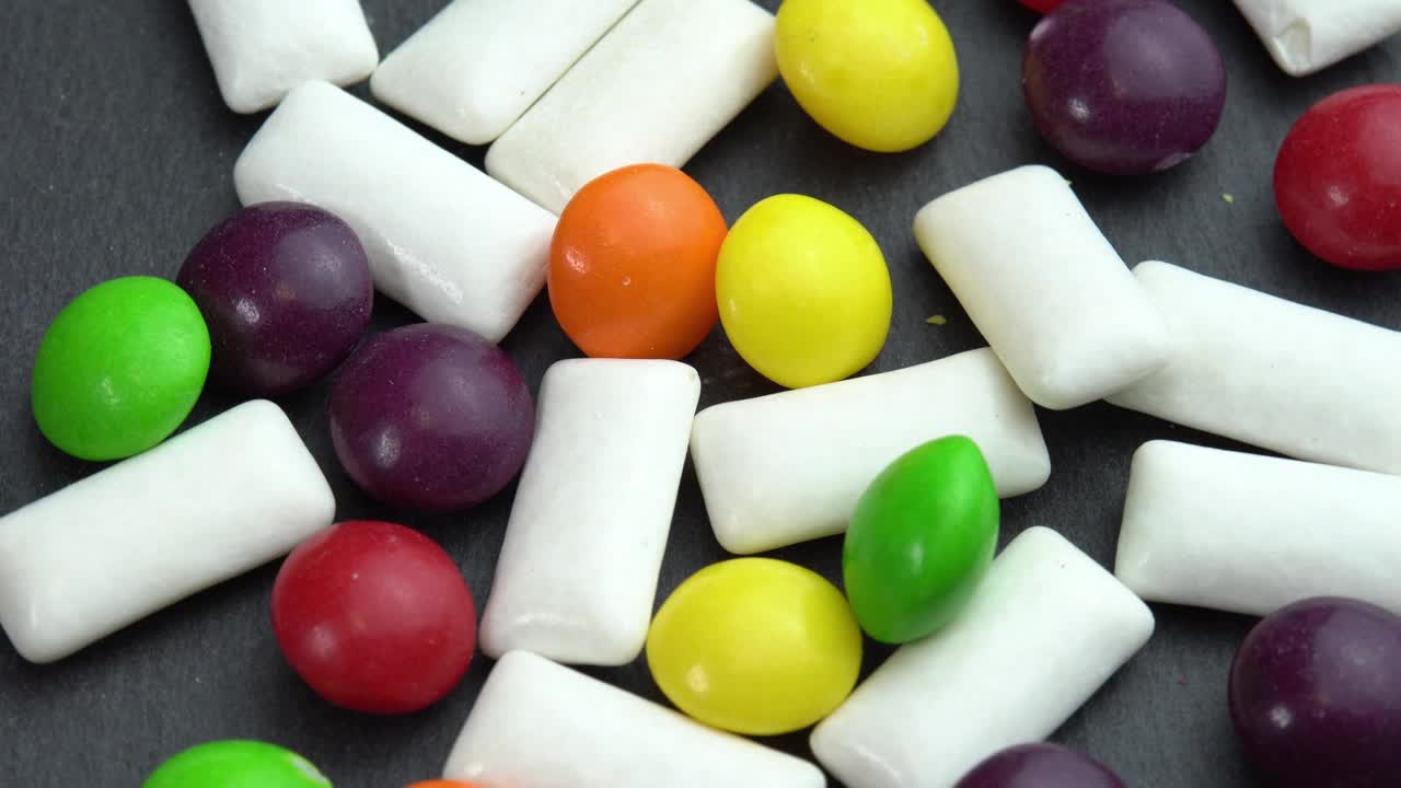 糖果彩色糖果彩虹糖和薄荷咀嚼垫，彩色糖果在黑色盘子上旋转视频下载